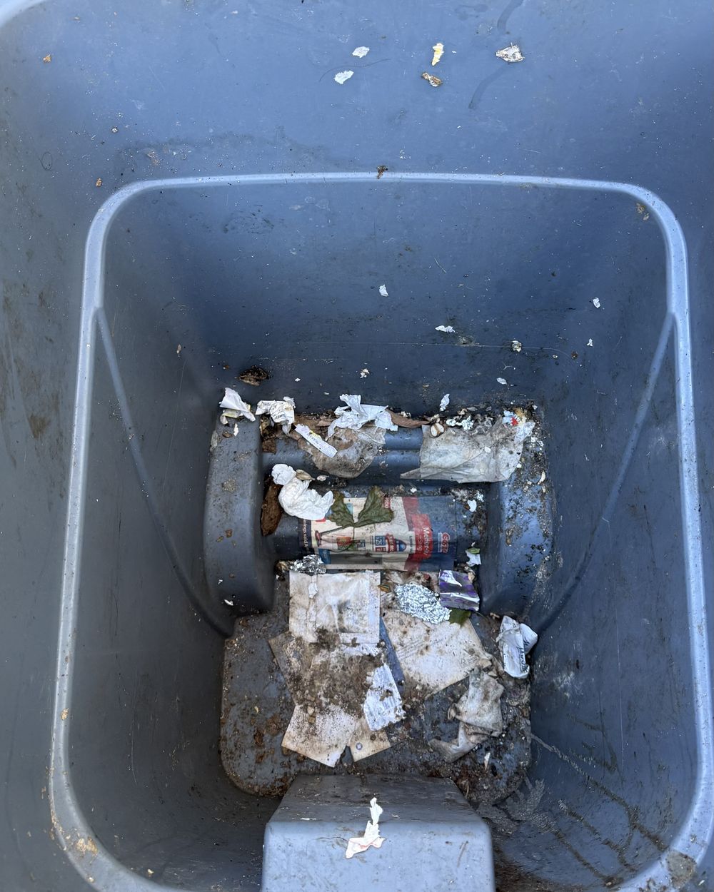 Inside of a trash bin before cleaning, with trash and grime stuck at the bottom.